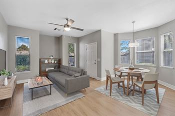 A living room with a grey couch, a coffee table, a dining table with chairs, and a ceiling fan.